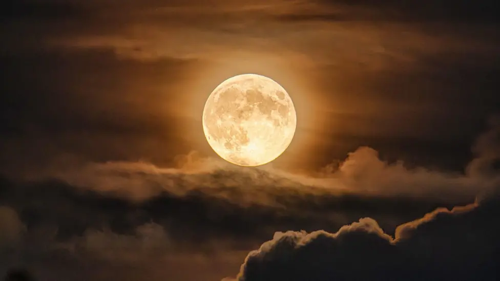 Hunter’s Moon glowing orange above clouds in the night sky