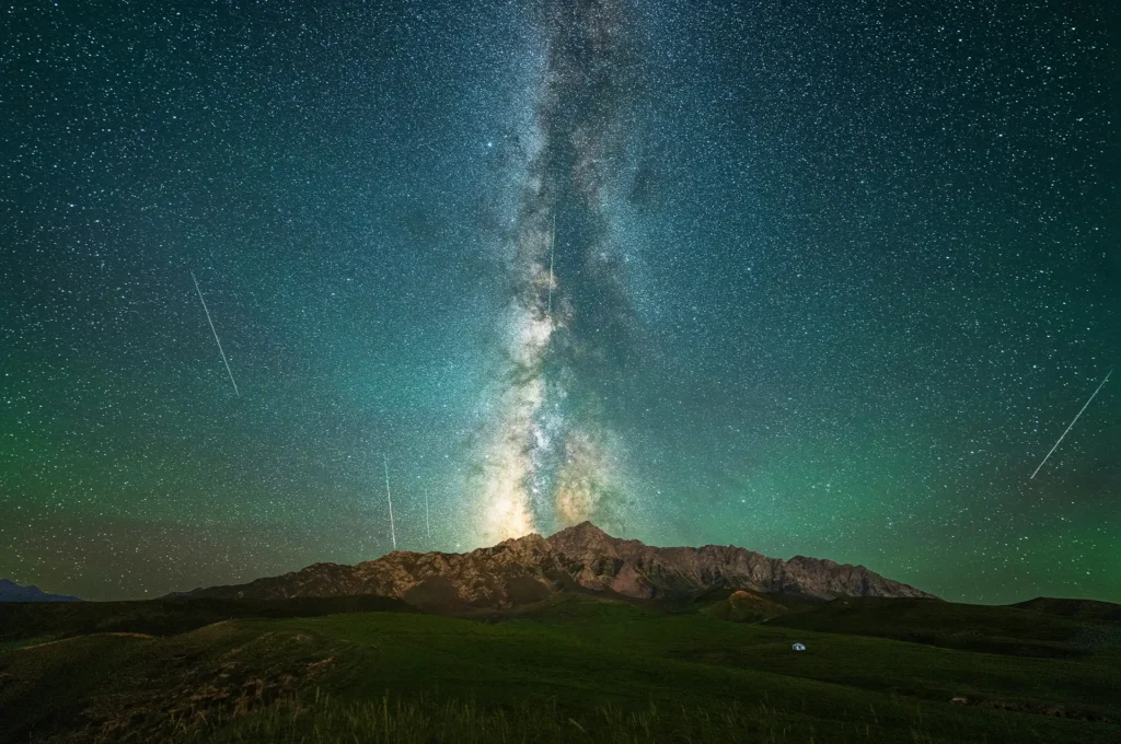 Milky Way and several meteors visible above mountains during a dark New Moon night