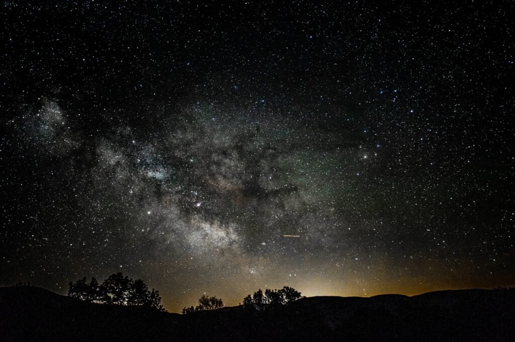 Milky Way stretching across a dark star-filled sky above silhouetted hills and trees