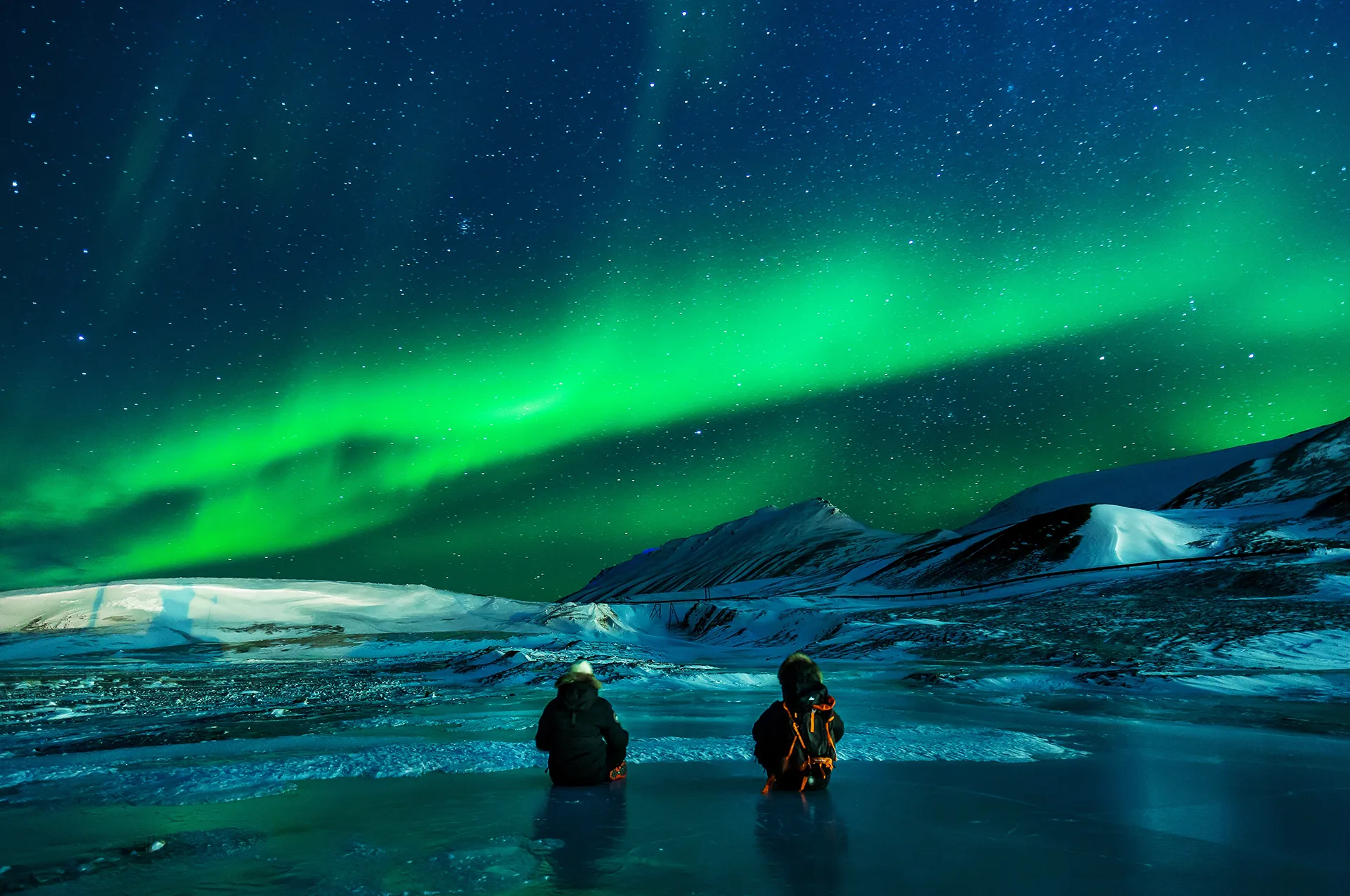 Stargazers watching the northern lights under a clear star-filled sky in a remote snowy landscape