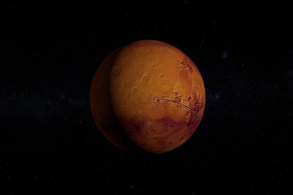 Mars showing its reddish surface and dark geological features against space